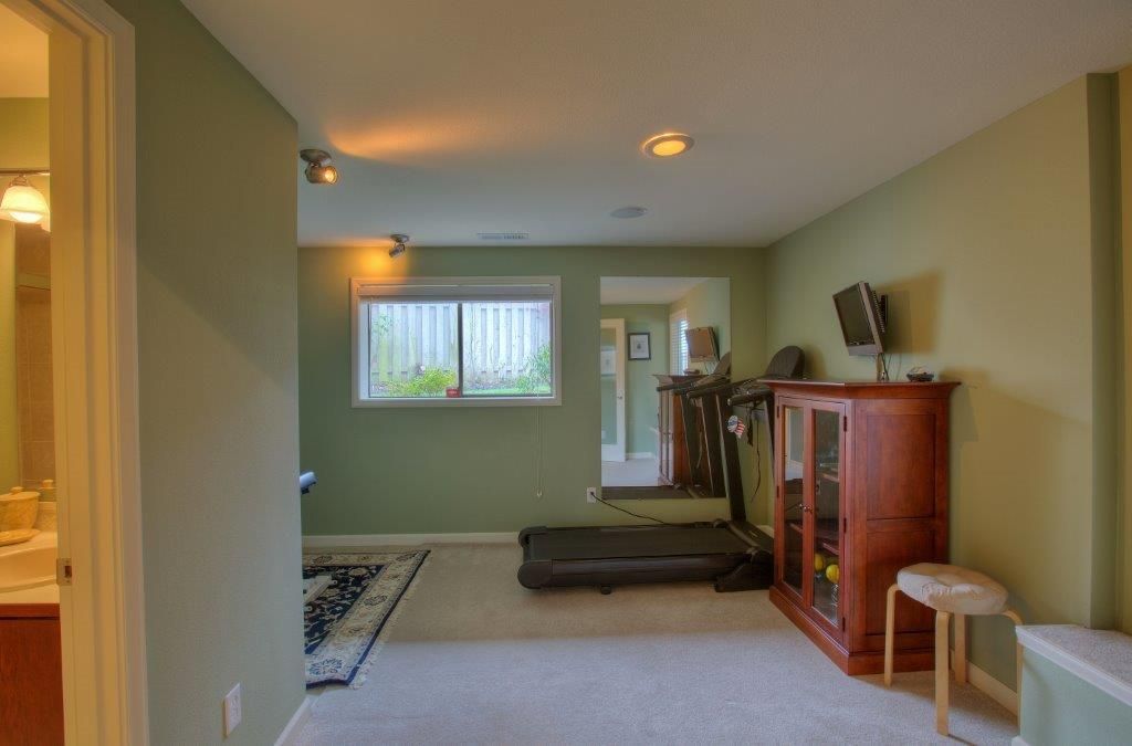 A small, green-walled home gym with a treadmill, cabinet, and a window.