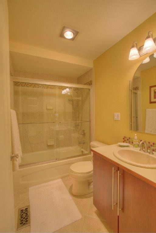 Bathroom with yellow walls, white fixtures, and a red vanity. Includes a tub/shower, toilet, and sink.