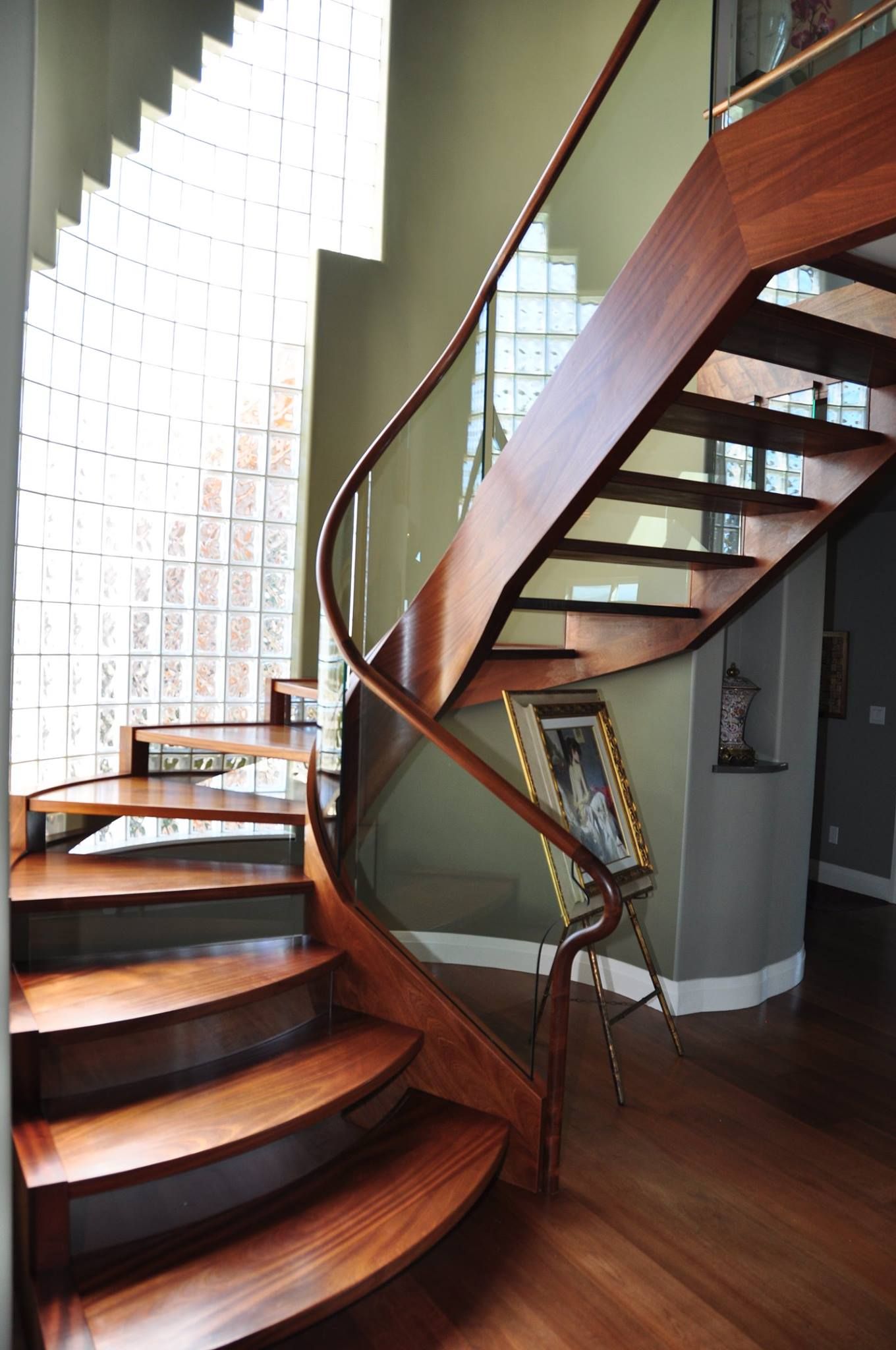 Wooden staircase with curved steps, glass railing, and a window of glass bricks.