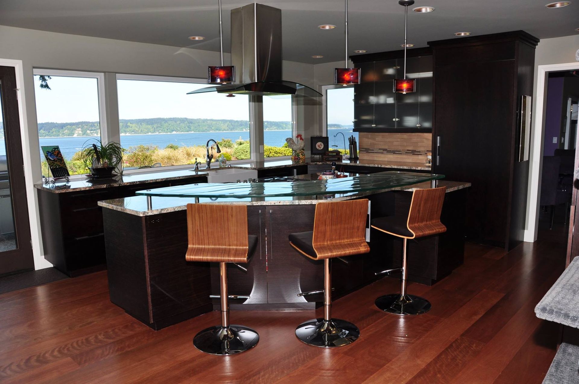 Modern kitchen with island, waterfront view, dark cabinets, wood floors, and bar stools.