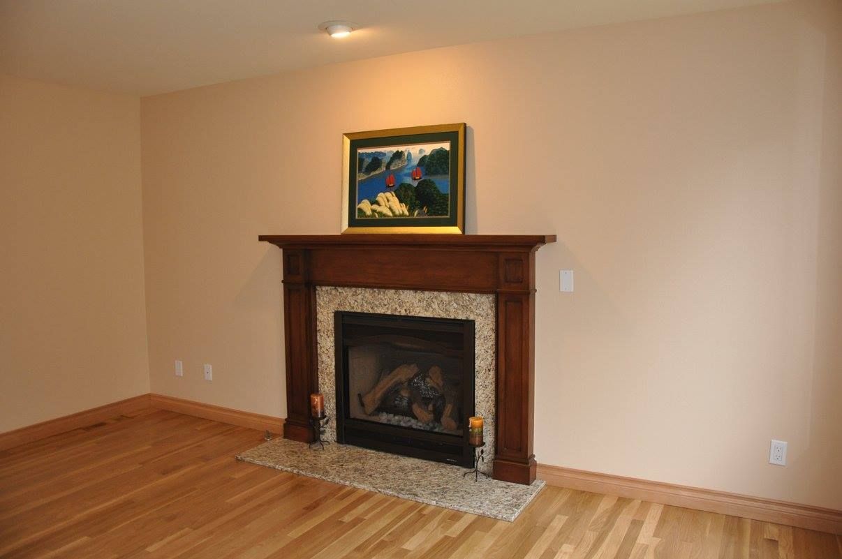 Fireplace with brown wood mantle, granite facing, and painting above it in a beige room.