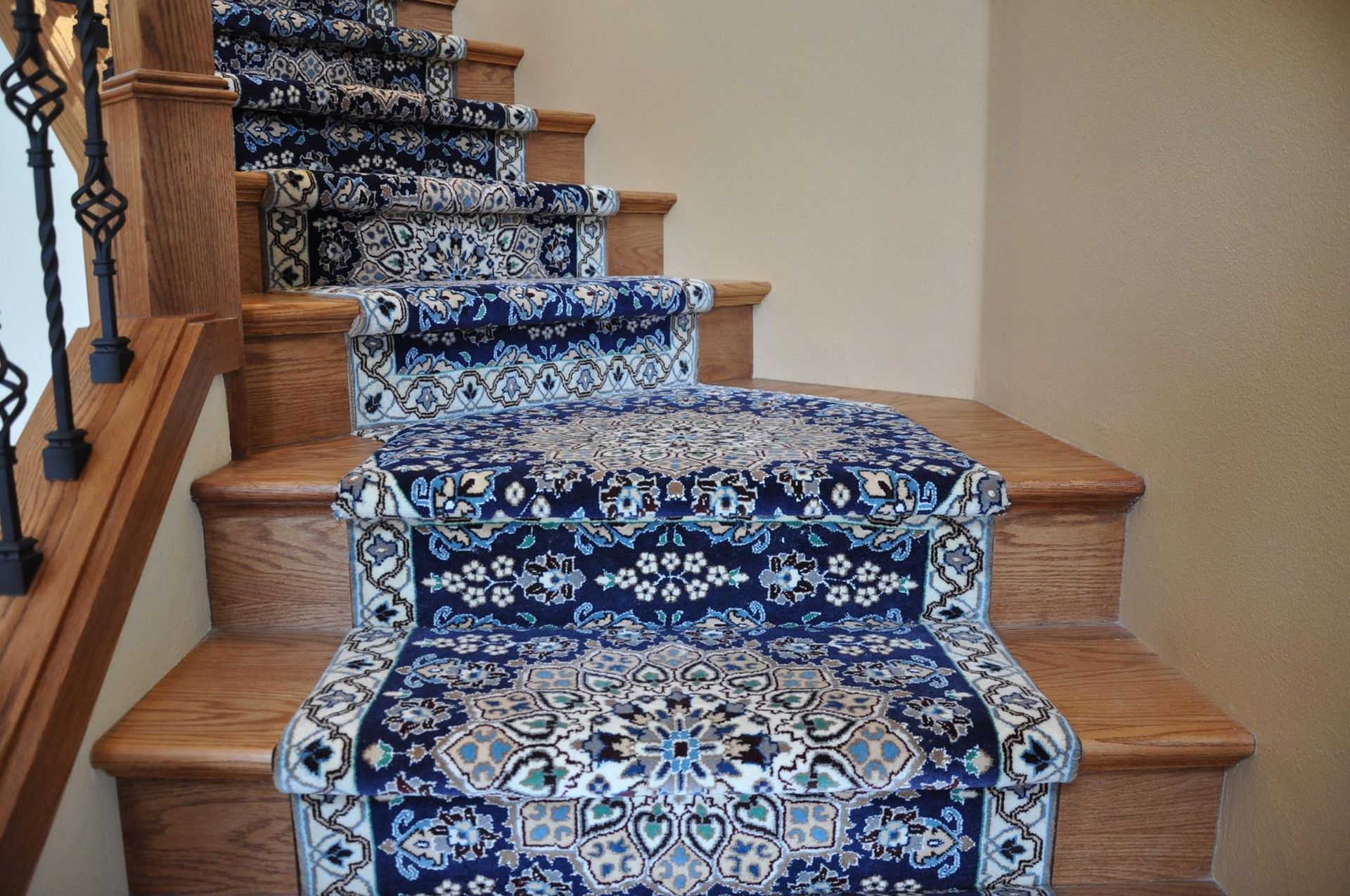 Blue patterned carpet runner on wooden stairs with a decorative metal railing.
