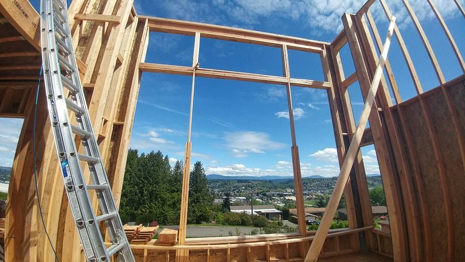 Framing of a house under construction, revealing a blue sky and distant cityscape through the window opening.