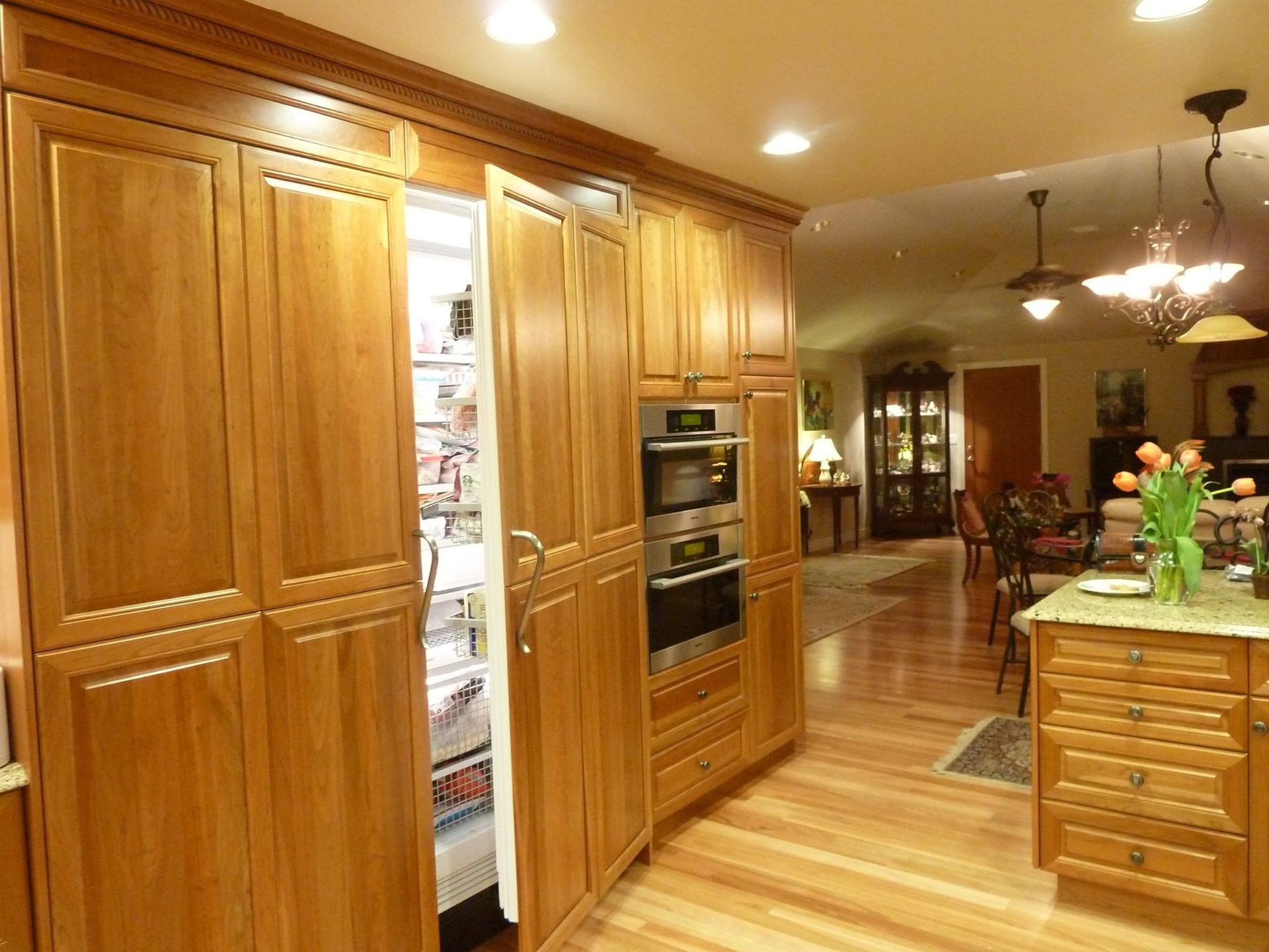 Kitchen with wooden cabinets, refrigerator open, and view into dining room.