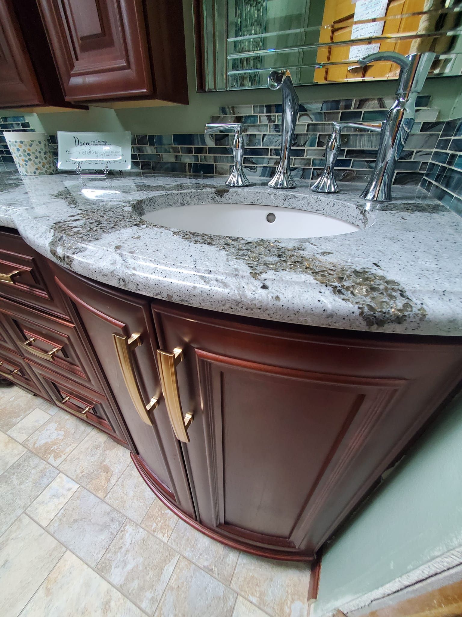 Bathroom vanity with curved dark wood cabinets, granite countertop, and dual chrome faucets.