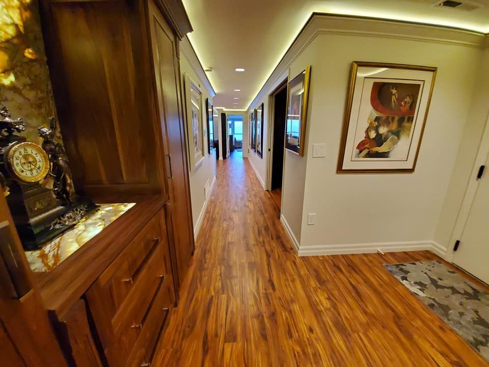 Long hallway with wood flooring, framed artwork, and overhead lighting.