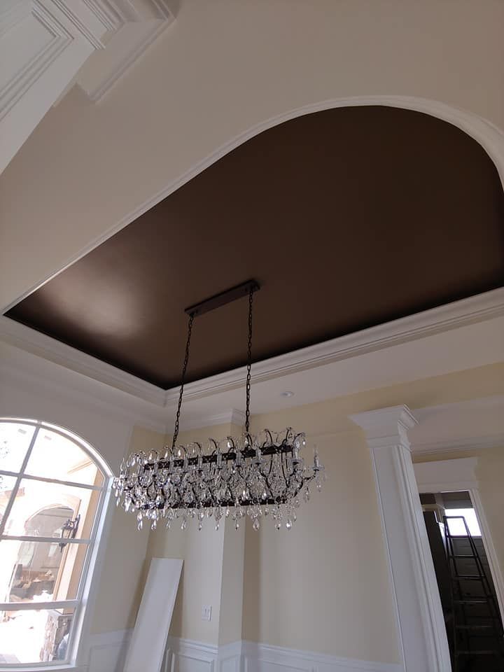 Chandelier hanging from brown arched ceiling with white molding and walls.