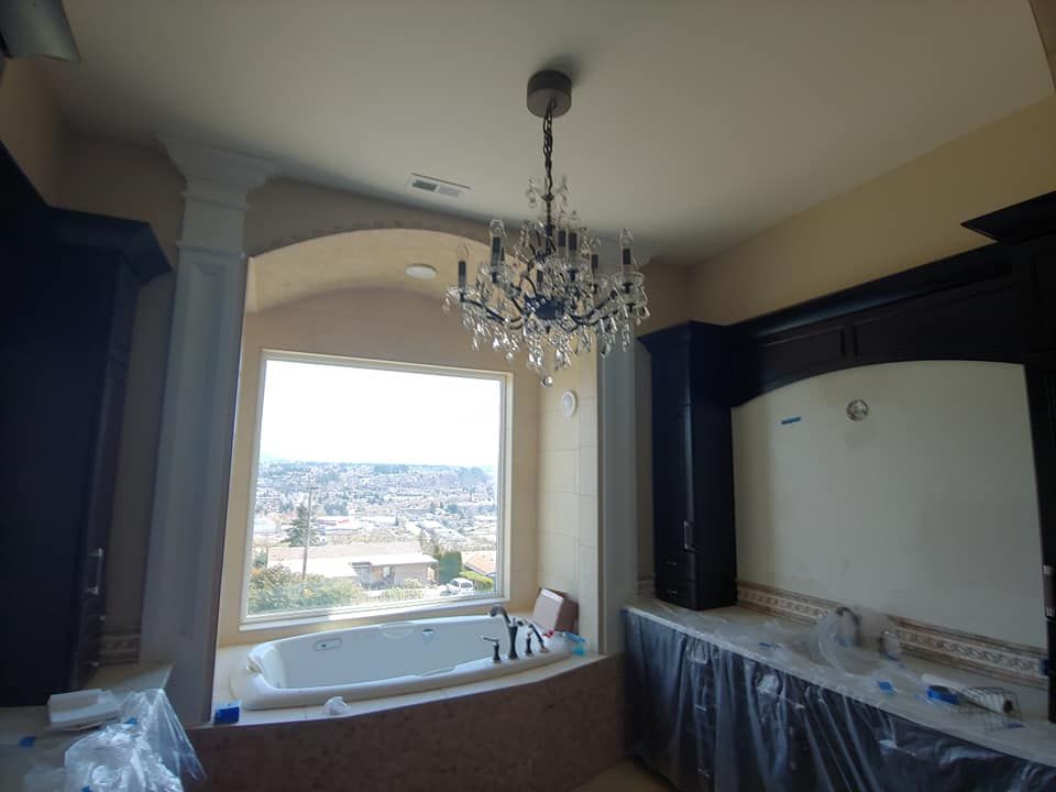 Bathroom with chandelier over a tub, overlooking a city view. Dark cabinetry and cream walls.