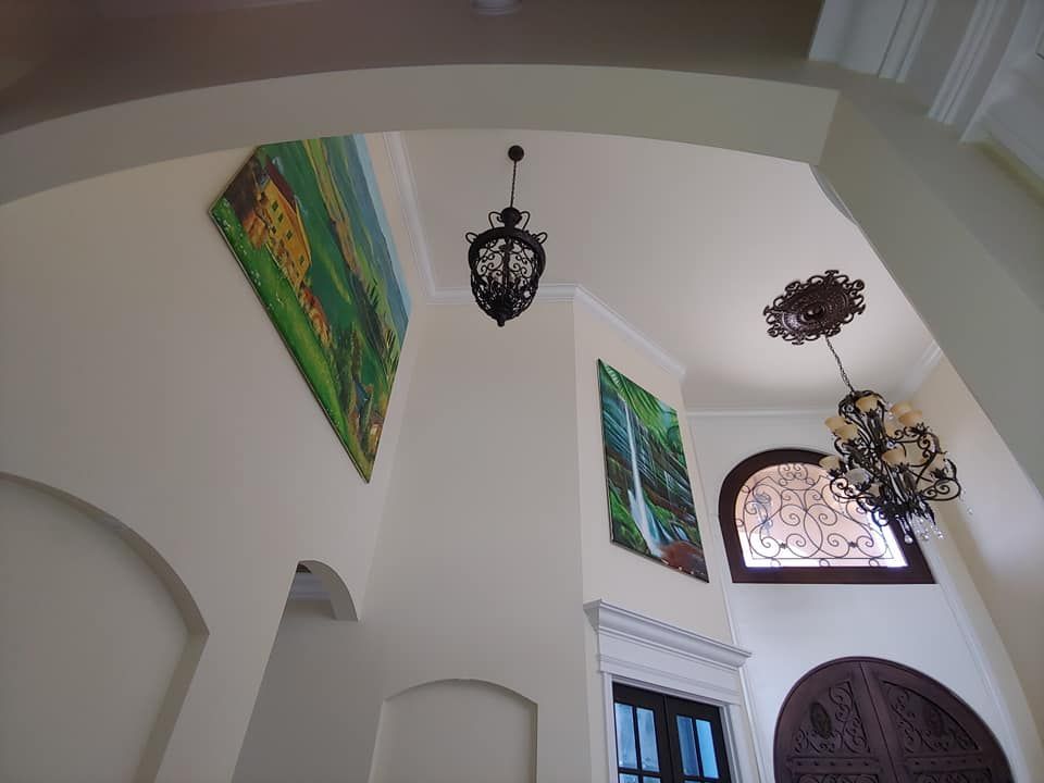 High-ceiling foyer with art, hanging lamps, and arched doorways. Cream walls, dark wood doors, and ornate details.
