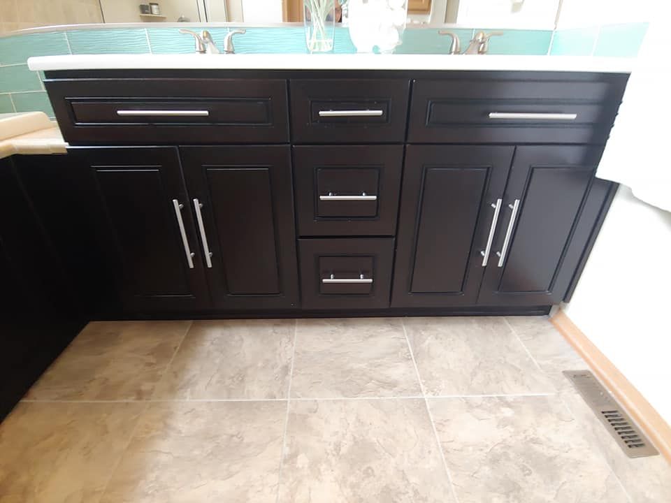 Dark brown bathroom vanity with silver handles and a white countertop; tile floor.