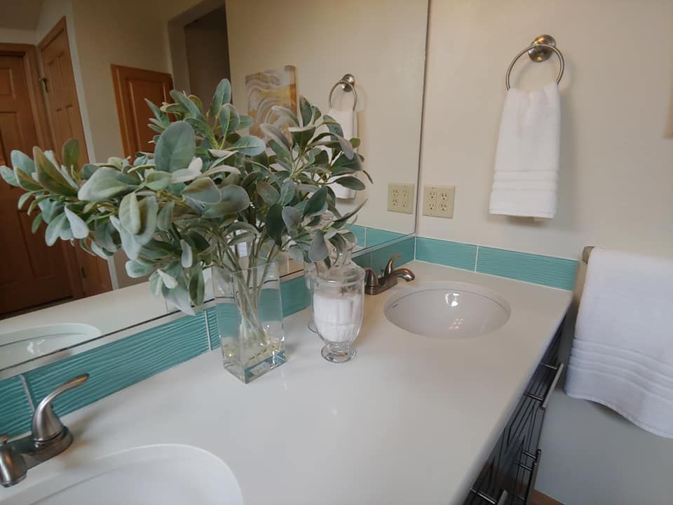 Bathroom counter with two sinks, a vase of greenery, and a towel rack with a white towel.