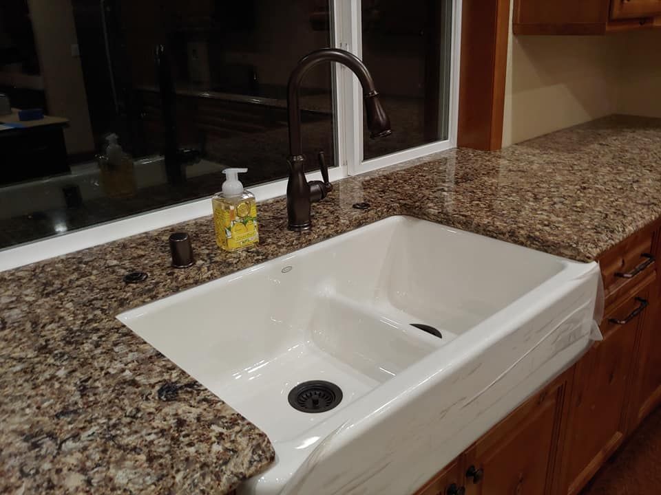 Kitchen sink with granite countertop, dark bronze faucet, and window behind.