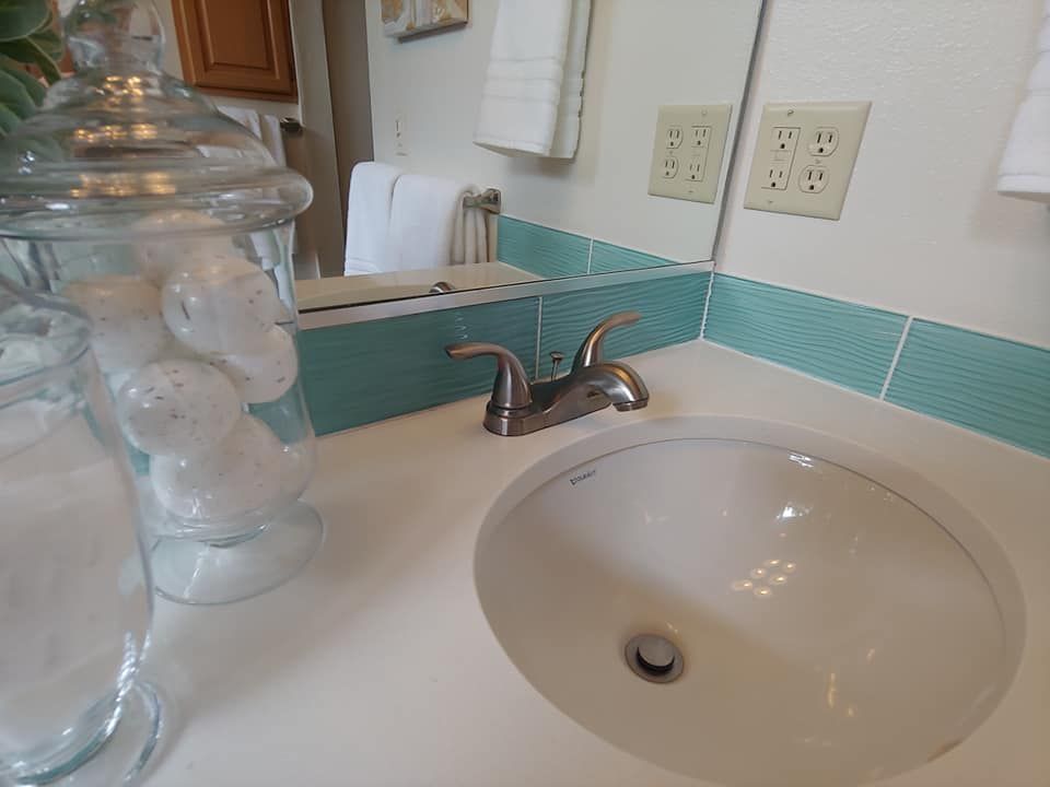 Bathroom sink with blue tile backsplash, mirror, and glass jars.