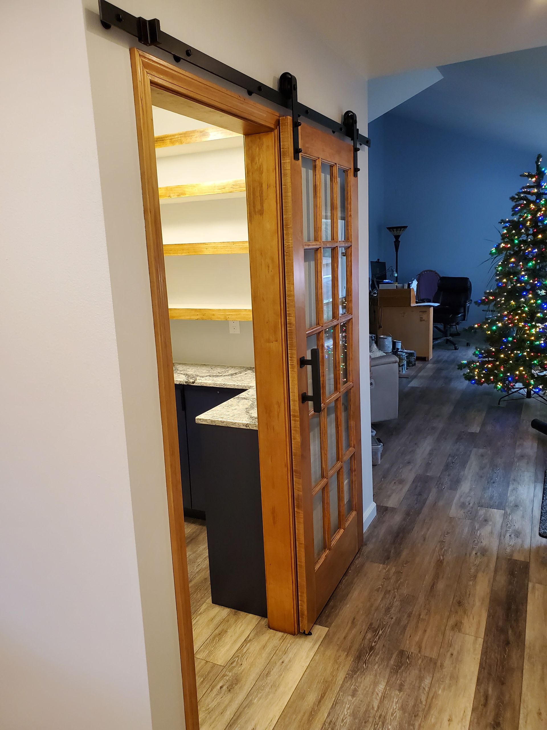 Barn door slides open to reveal a pantry with shelves and countertop; Christmas tree visible.