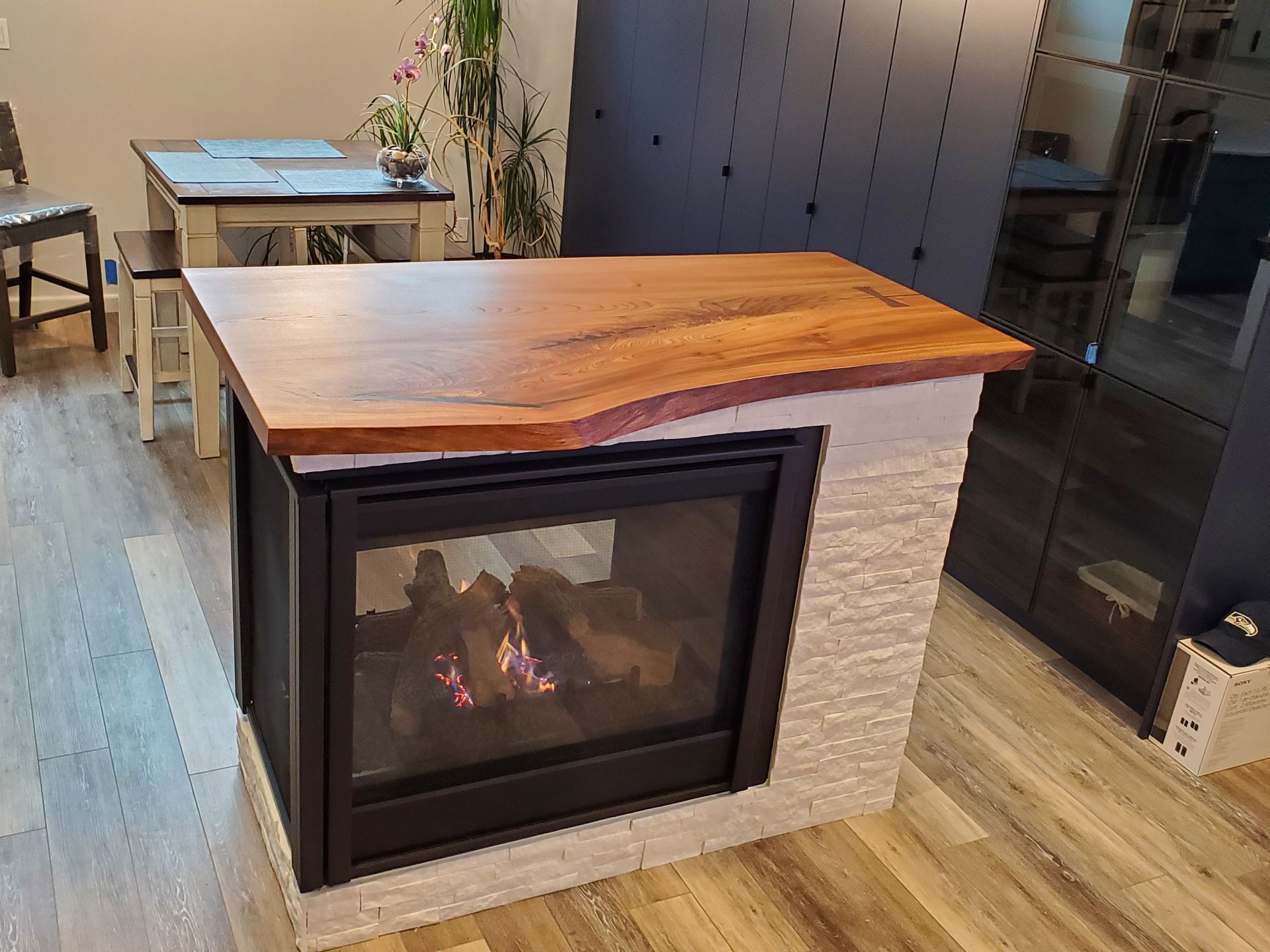 A modern fireplace with a wooden countertop and tiled sides, flames visible in the center.