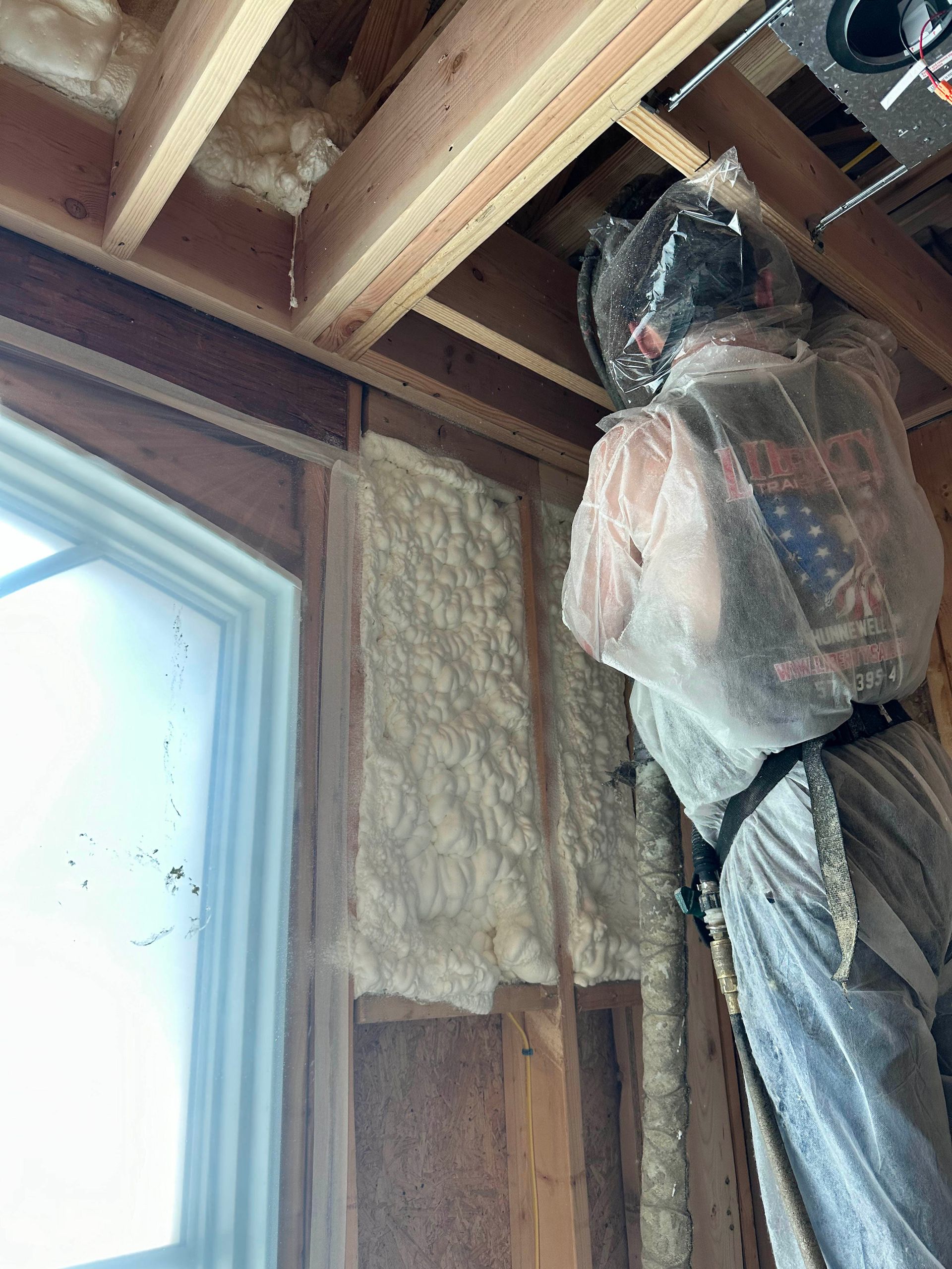 A man is spraying insulation on a wall in a house under construction.