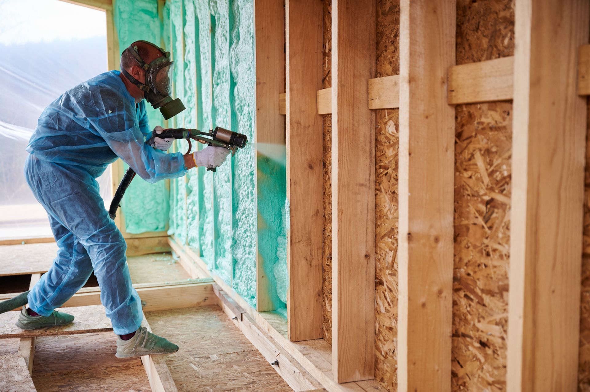 A man is spraying insulation on a wooden wall.