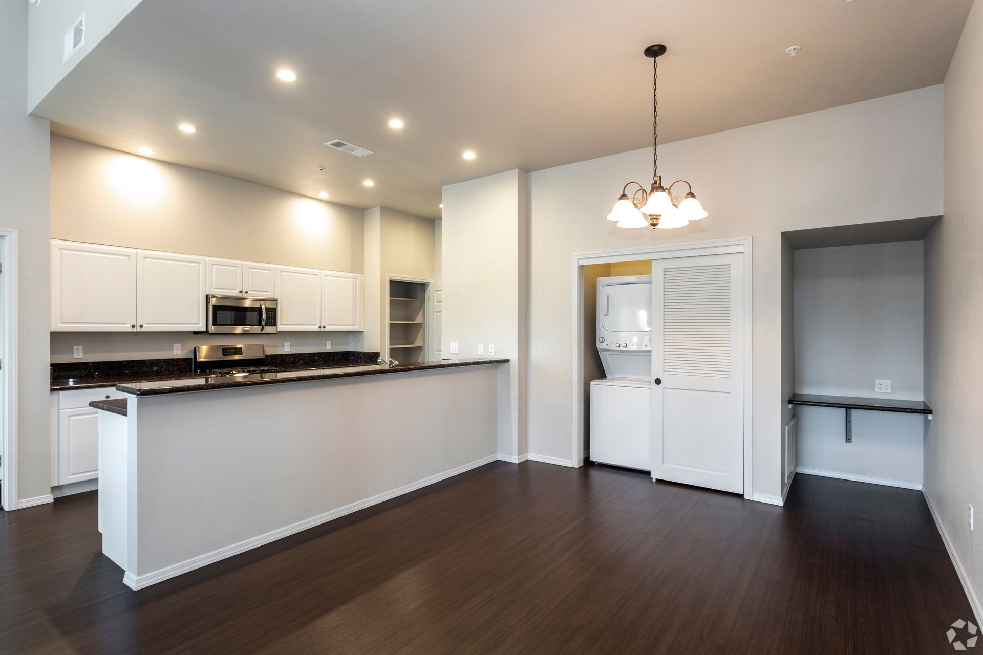 Modern kitchen with white cabinets, dark countertops, and a built-in washer/dryer unit. Dark wood floor.