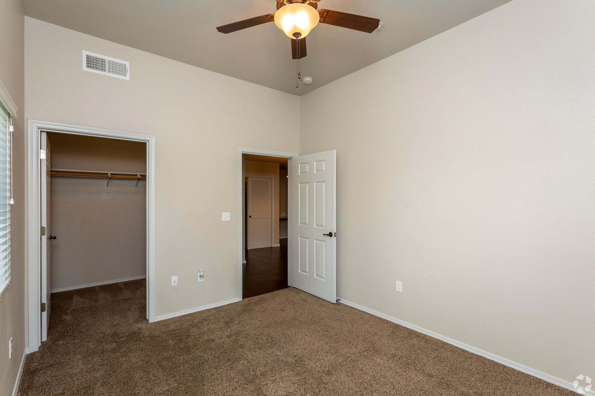 Empty bedroom with tan walls, brown carpet, open closet, and a ceiling fan.