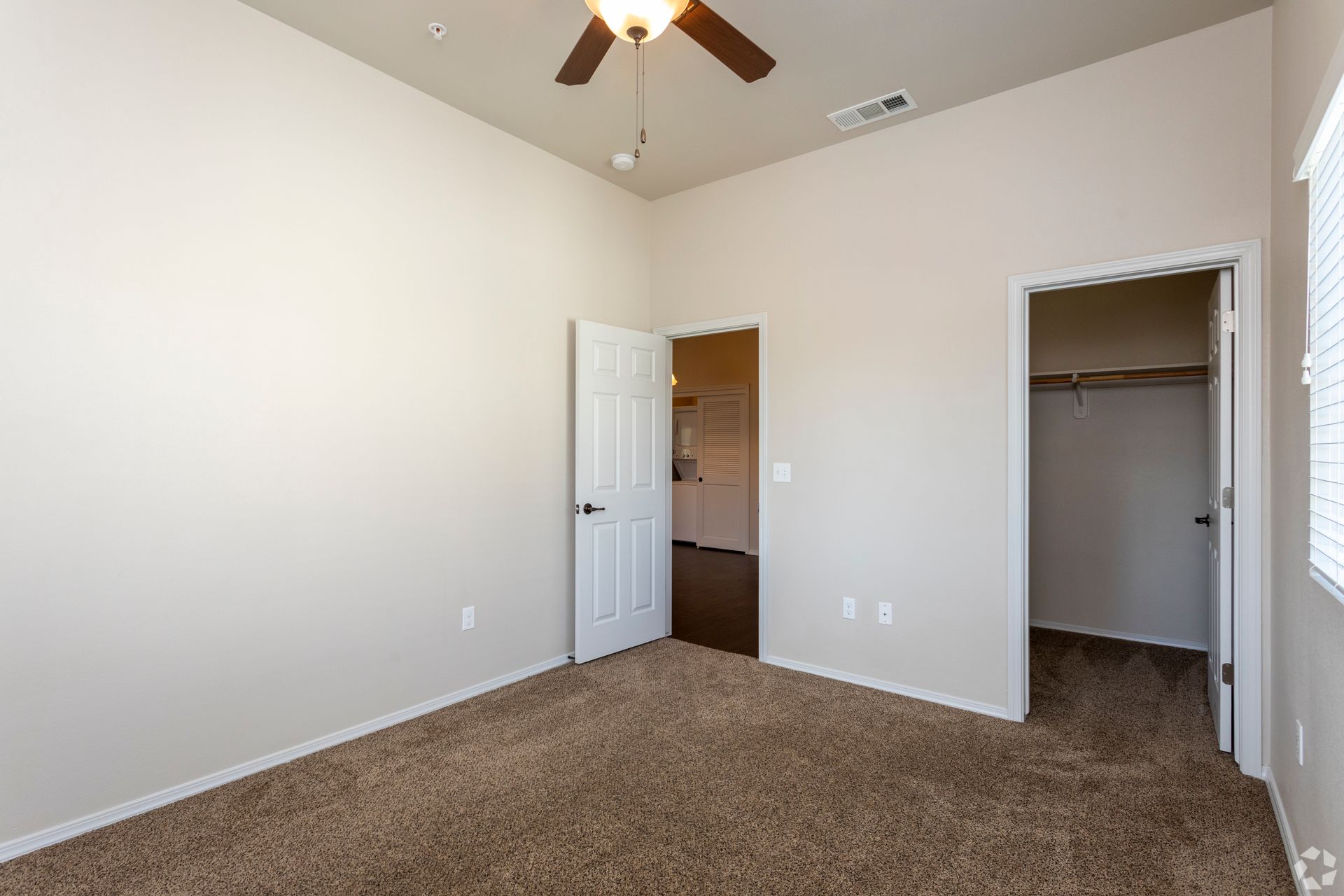 Empty bedroom with brown carpet, open closet, and door to another room.