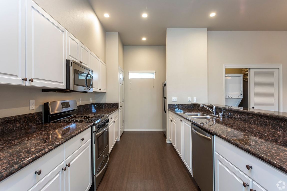 Bright kitchen with white cabinets, stainless steel appliances, and dark countertops.