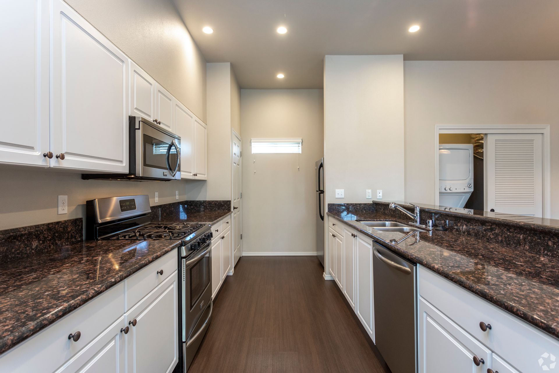 Bright kitchen with white cabinets, stainless steel appliances, and dark countertops.