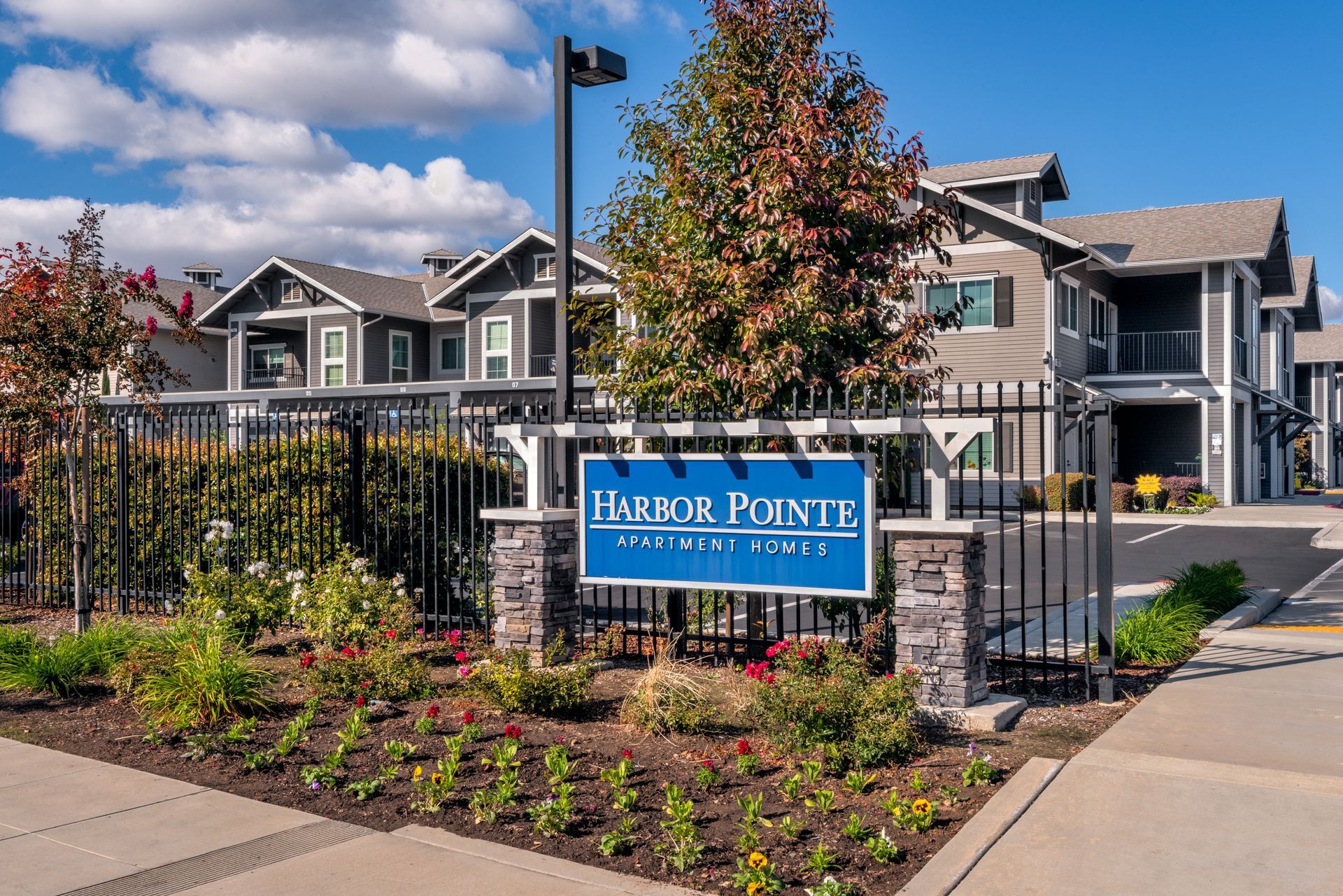 Harbor Point apartment complex entrance sign, brick, black fence, with buildings and foliage.