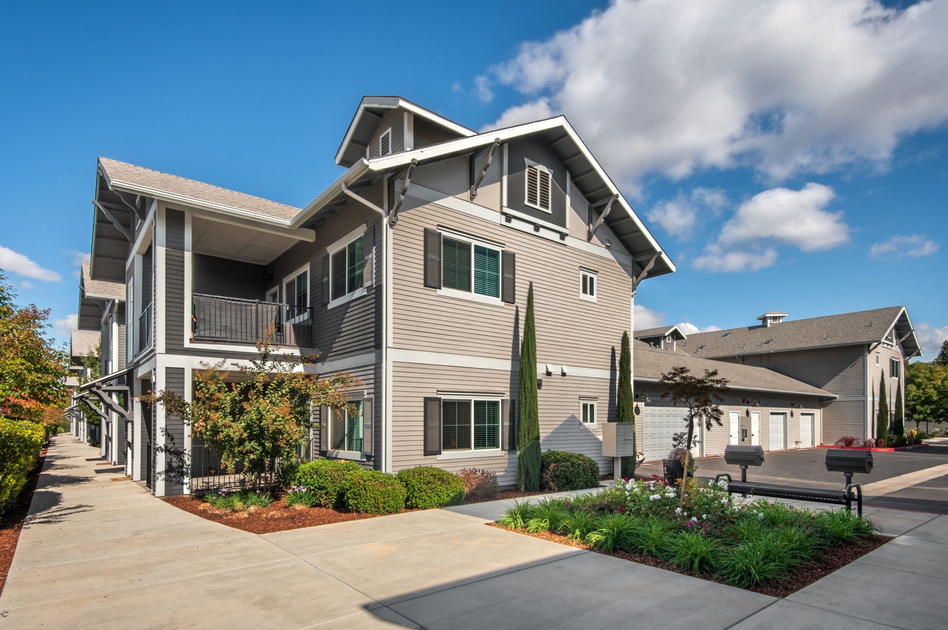 Multi-story building with gray siding, black shutters, blue sky, and a sidewalk.