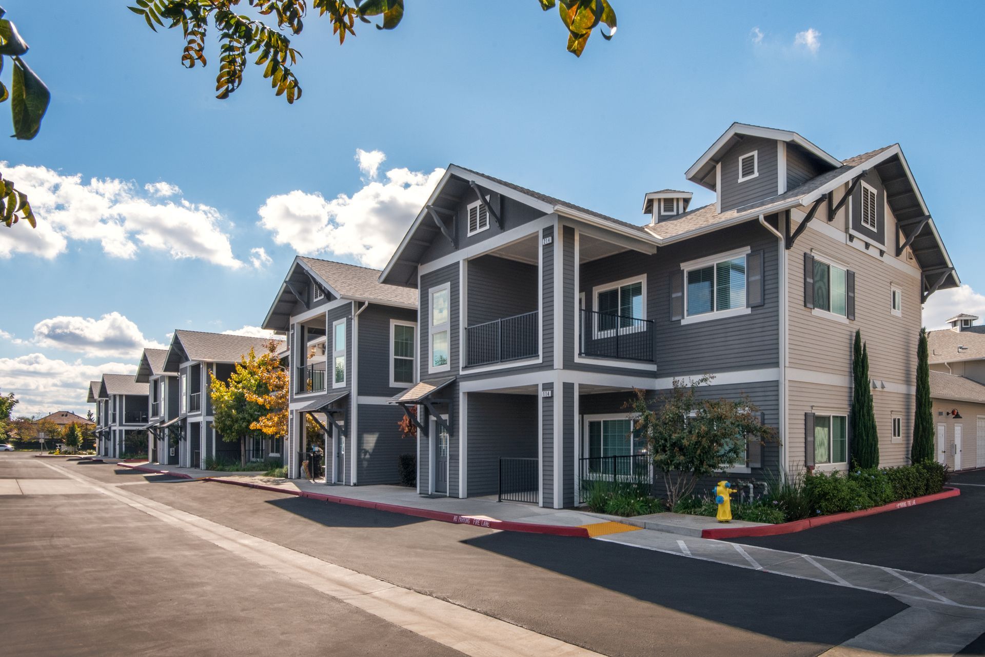 Row of modern gray townhouses with balconies, under a blue sky.