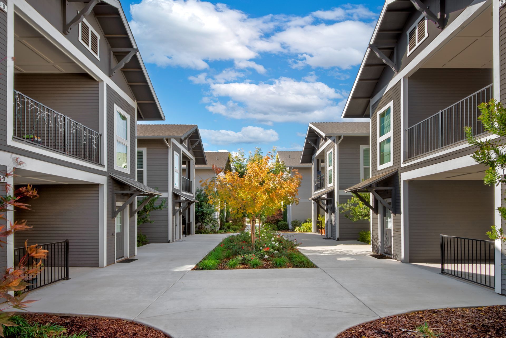 Gray apartment complex courtyard with a tree and blue sky.
