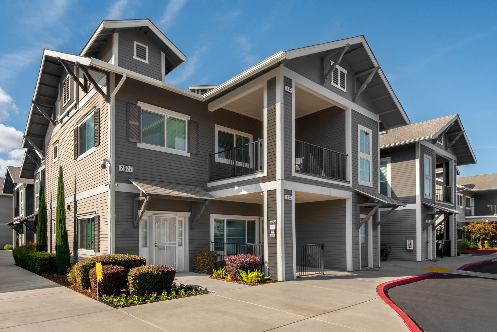 Grey apartment building with balconies, blue sky, and landscaping.