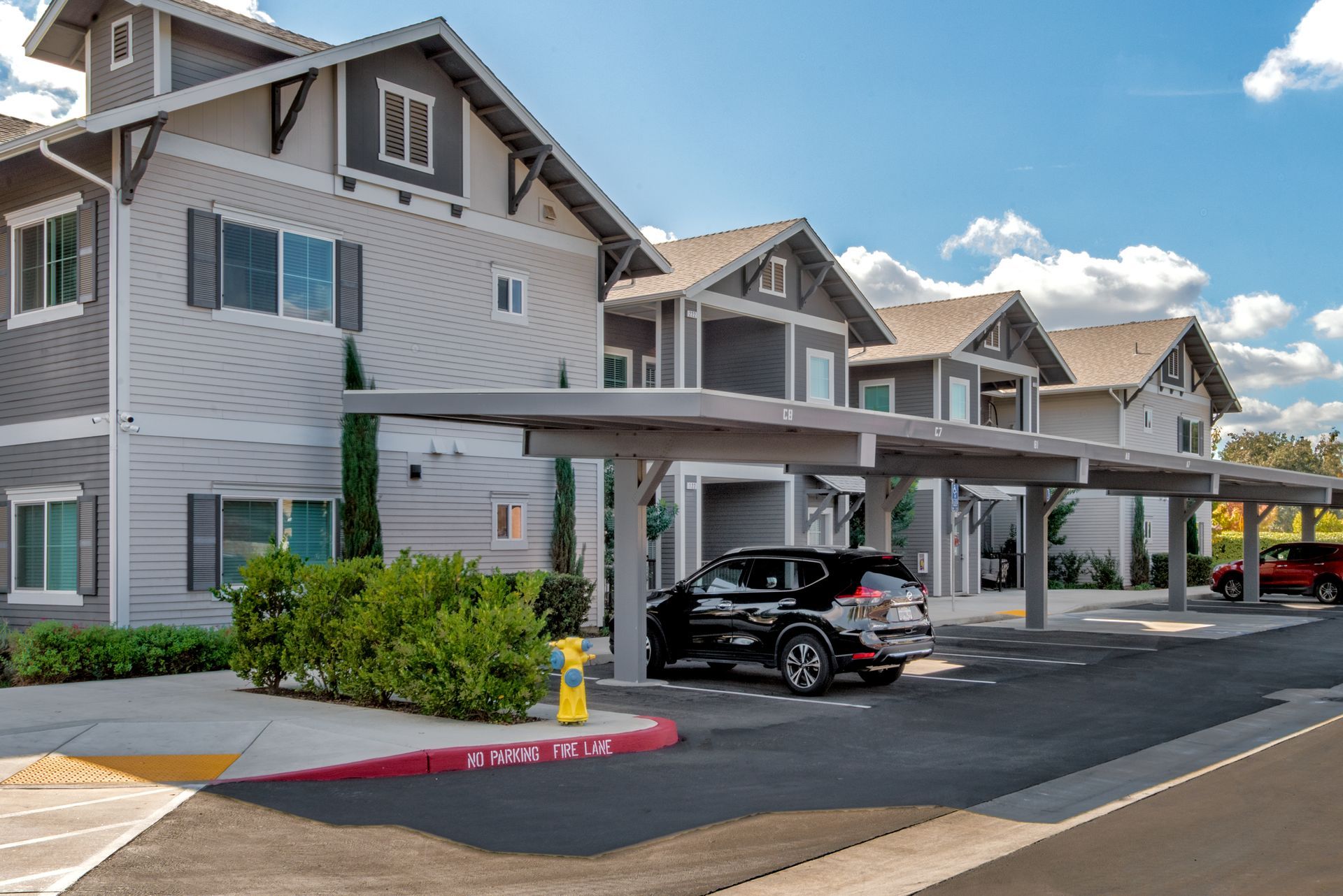 Gray apartment complex with carports, a car parked beneath, and a blue sky.