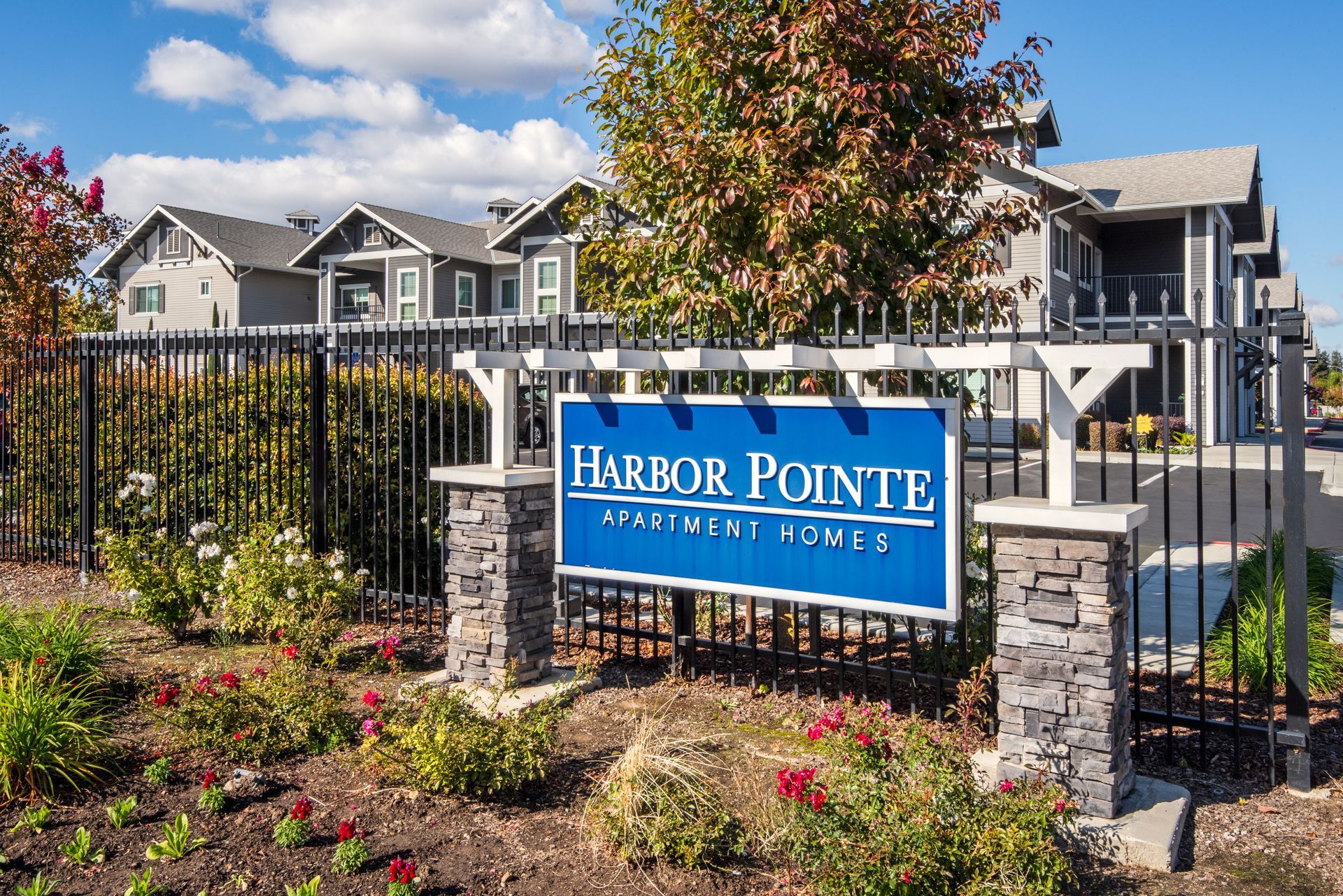 Sign for Harbor Pointe Apartment Homes with buildings and landscaping behind a black metal fence.