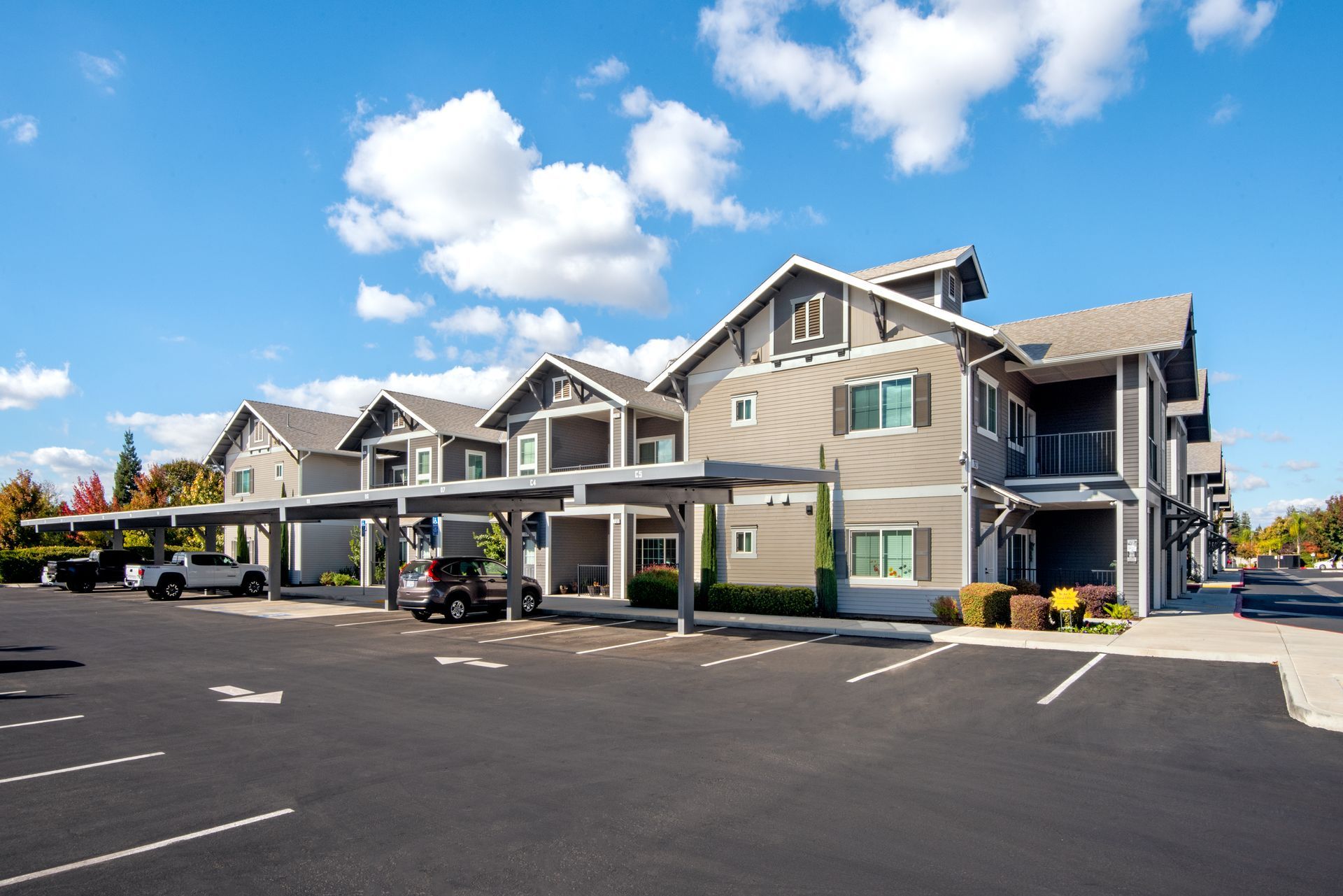 Apartment complex with covered parking, gray siding, and blue sky.