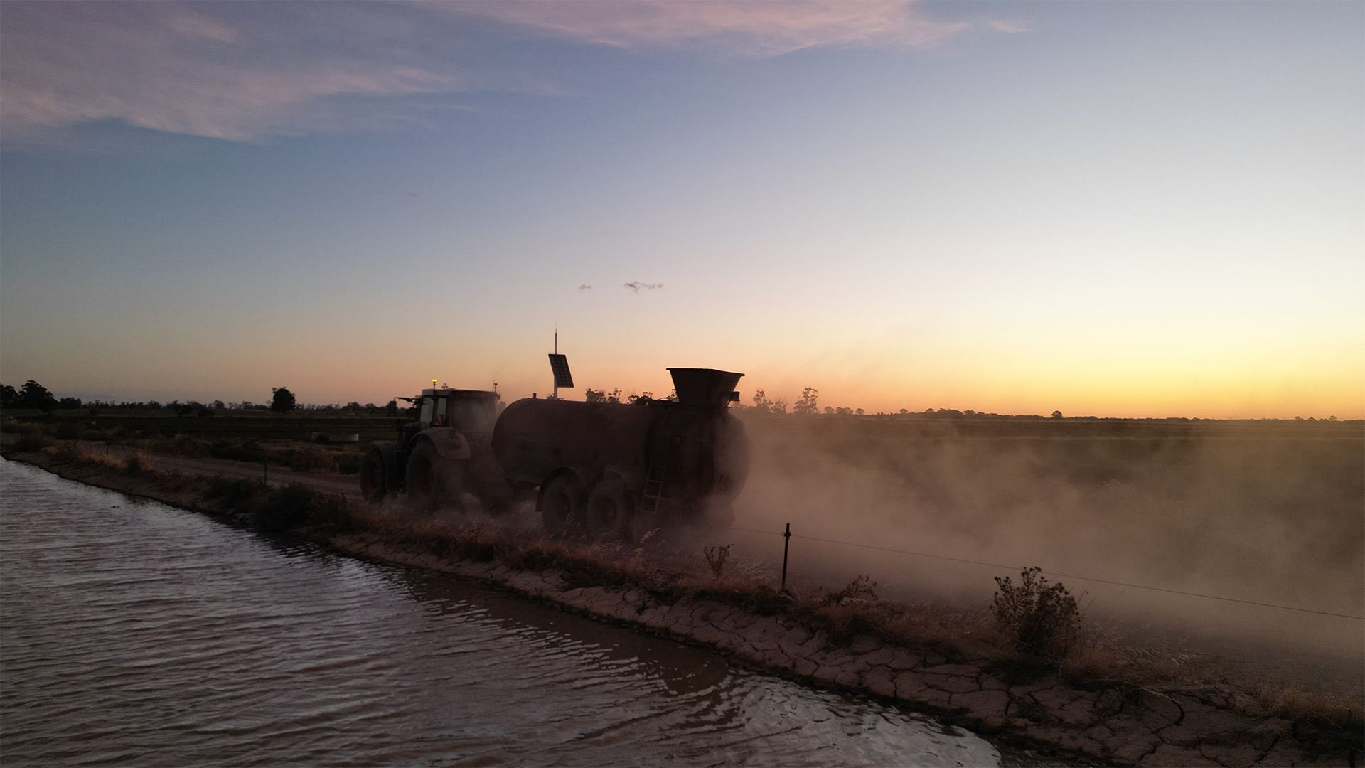 a tractor is plowing a field near a body of water at sunset