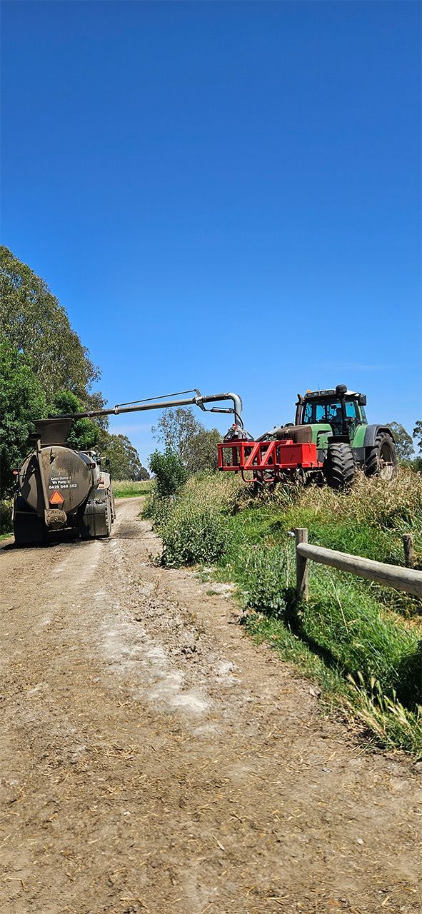 a tractor is loading hay into a trailer on a dirt road .