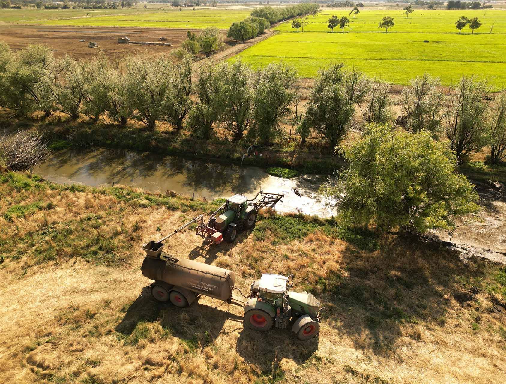 an aerial view of two tractors in a field next to a river .