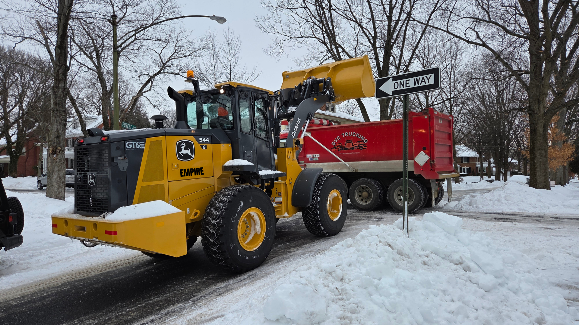 Yellow wheel loader dumps snow into a red DVC dump truck.