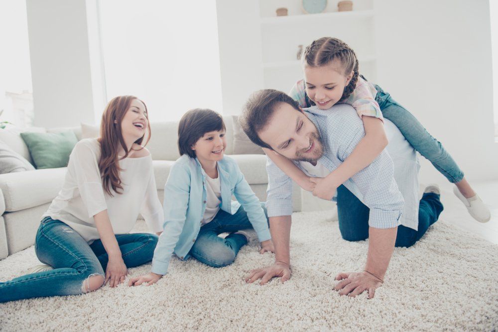 Happy Family Sitting On A Carpet Floor — Flooring Supply & Installation In Laurieton, NSW