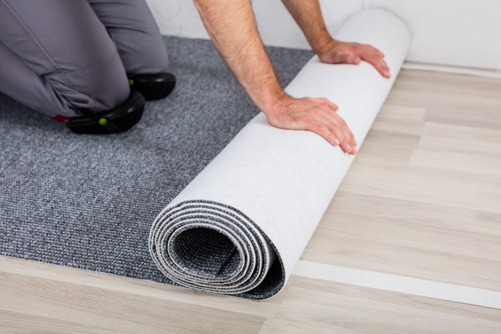 Close-up Of Worker's Hands Unrolling Carpet On The Floor — Flooring Supply & Installation In Port Macquarie, NSW