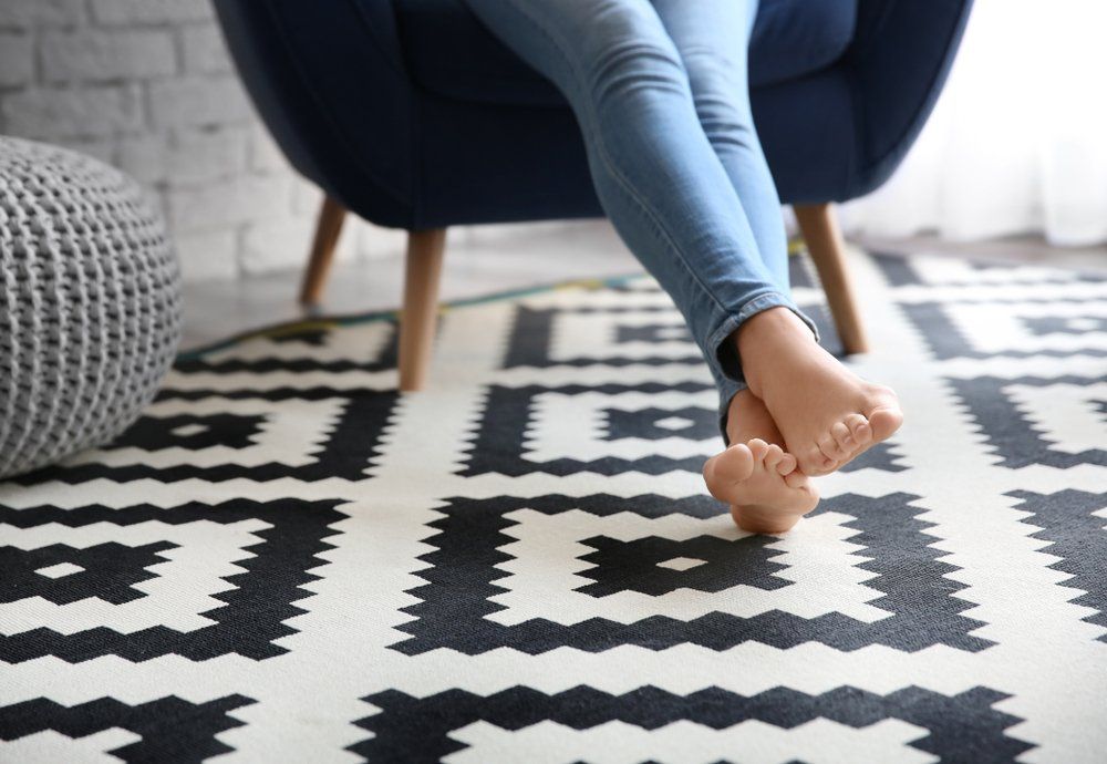 Woman Sitting In Armchair With Feet On Carpet at Home — Flooring Supply & Installation In Laurieton, NSW