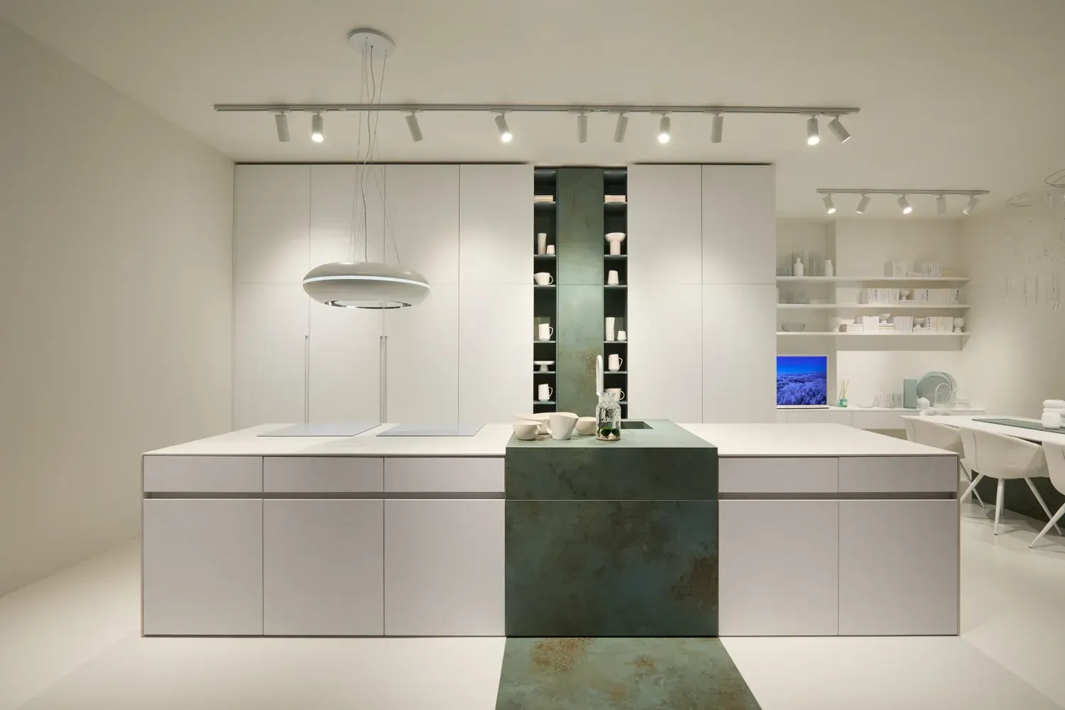 Moderna cucina bianca con grande isola, pannello decorativo verde acqua e mensole integrate. Illuminazione a soffitto e lampada a sospensione.