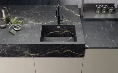 Piano di lavoro scuro con lavandino integrato, impreziosito da venature dorate. Un rubinetto nero è posizionato sopra il lavandino.