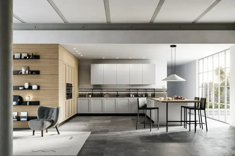 Cucina moderna con mobili in legno chiaro e bianchi, isola centrale con sgabelli e finestra. Pavimento grigio e travi a vista sul soffitto.