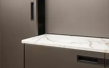 Piano di lavoro grigio e bianco con effetto marmo, sopra un mobile coordinato. Maniglia e mobile scuri sulla sinistra.