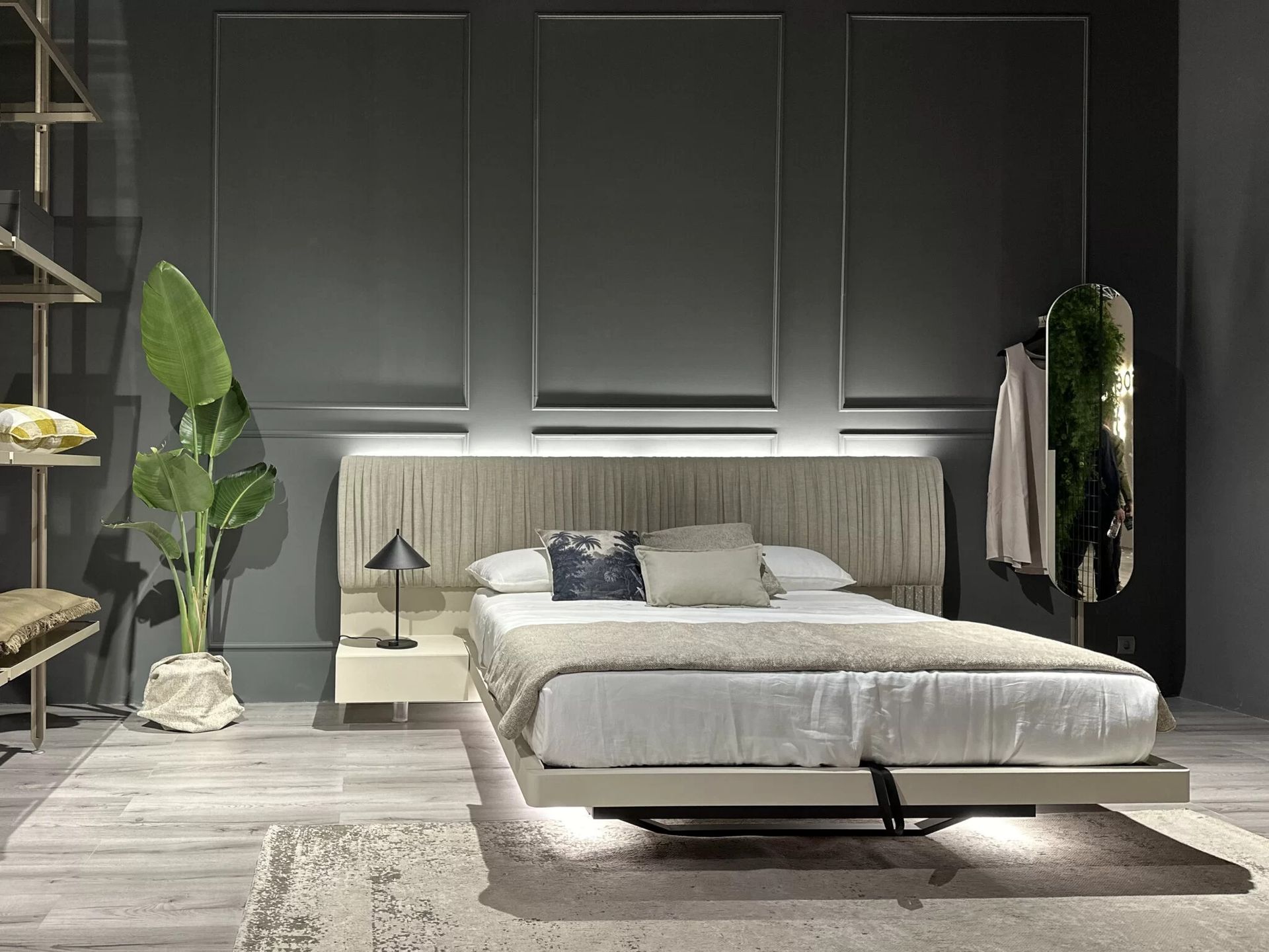Camera da letto moderna con letto a piattaforma, toni neutri e pannelli decorativi alle pareti. Una pianta alta e uno specchio aggiungono accenti.