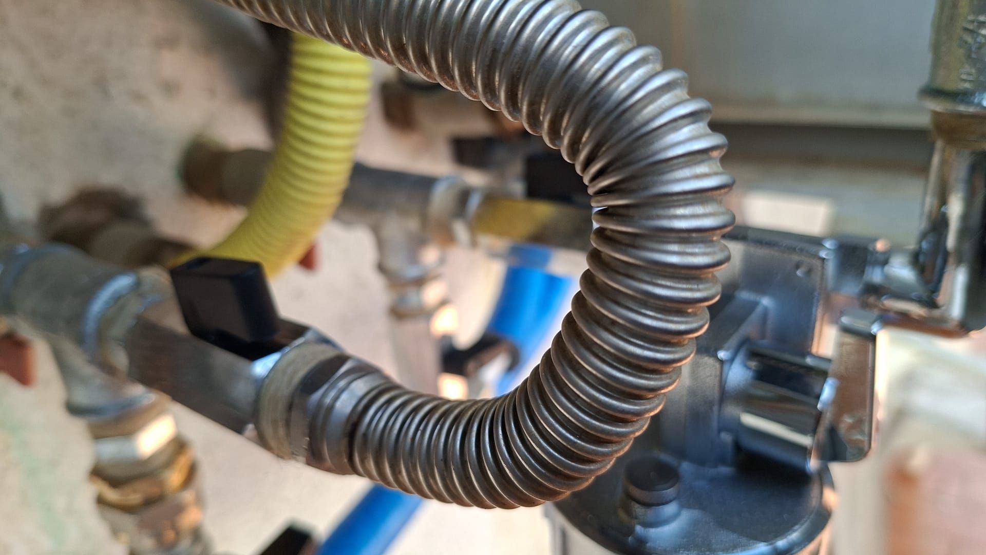 Primo piano di un tubo flessibile metallico corrugato e dei relativi raccordi su un macchinario industriale.