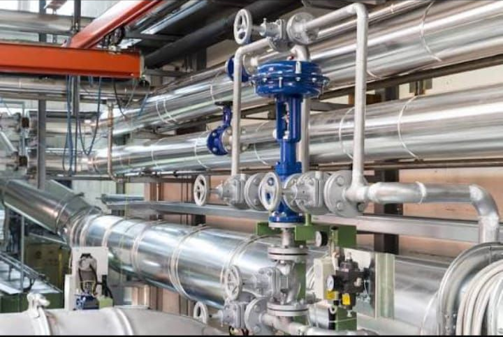 Tubature industriali e valvole blu all'interno di uno stabilimento produttivo lucido.