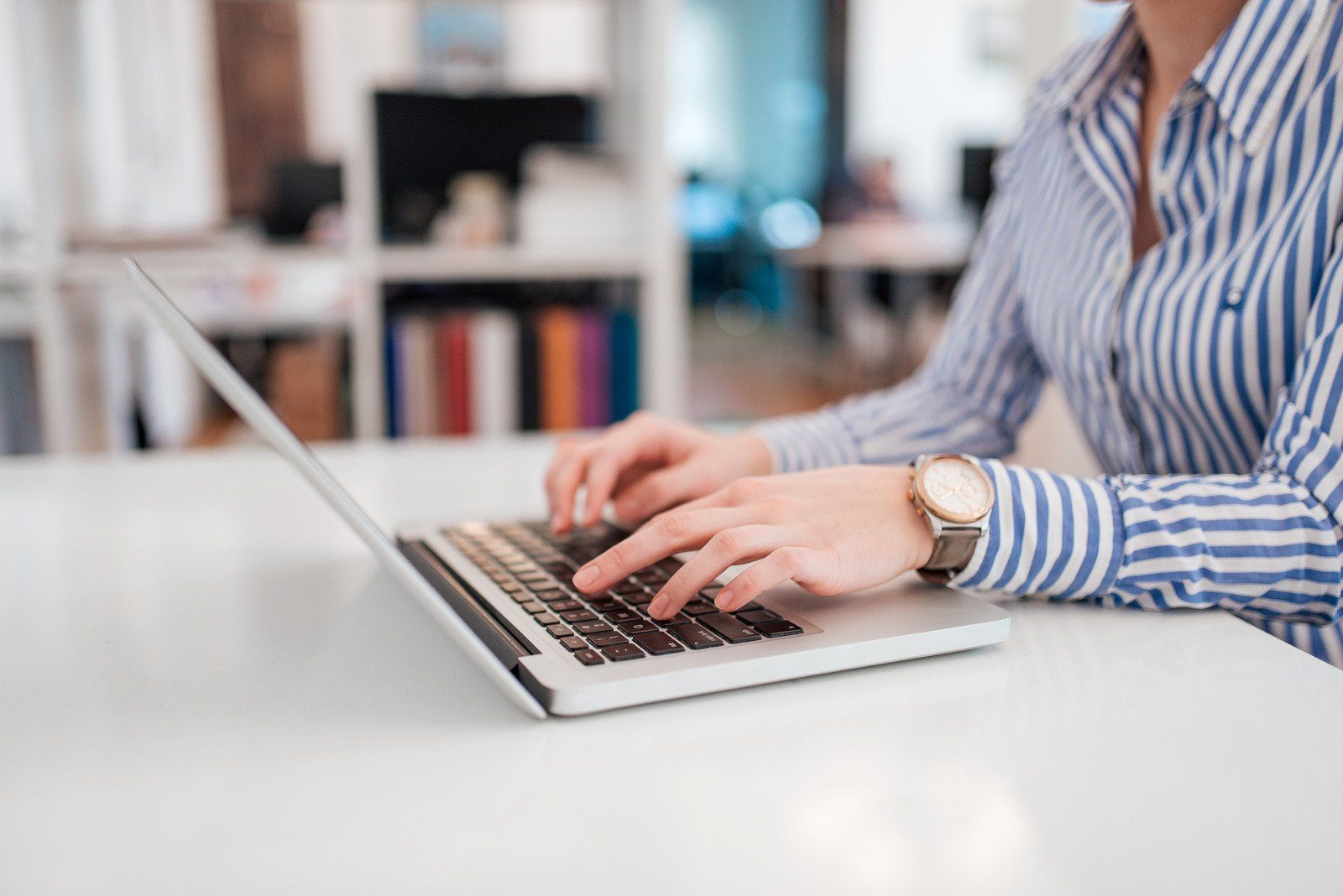 A woman is typing on a laptop computer at a desk.