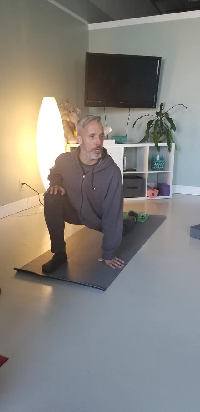 A man is squatting on a yoga mat in a living room.